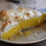 Imahem de uma torta de limão ainda na forma: massa fina, creme amarelo de limão e merengue de suspiro dourado. A torta está cortada no meio.