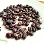 Imagem de vários grãos de café torrados, sobre um fundo branco.