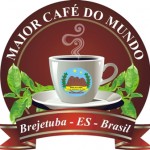 Desenho de uma xícara de café com fumaça saindo, rodeada de folhas. O desenho tem um circulo de fundo, com os dizeres "Maior café do mundo" e, sob a xícara, uma faixa com as palavras "Brejetuba - ES - Brasil".
