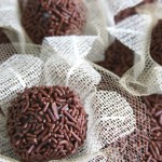 Imagem de brigadeiros sobre forminhas de gaze bege claras, cortadas em forma de flor e cobertas com tule quase transparente. Os brigadeiros estão sobre um fundo de chocolate granulado